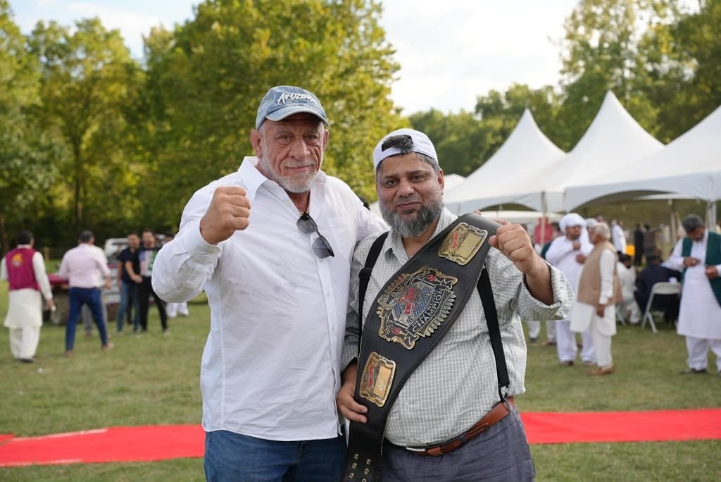 Dr. Ahmed Ejaz holding a championship belt beside a friend at an outdoor community event