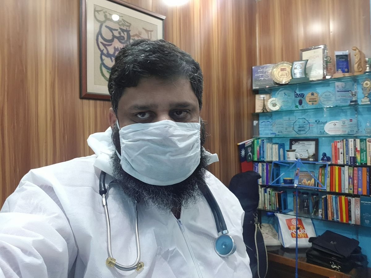 Dr. Ahmed Ejaz in a protective gown and mask with a stethoscope in his office