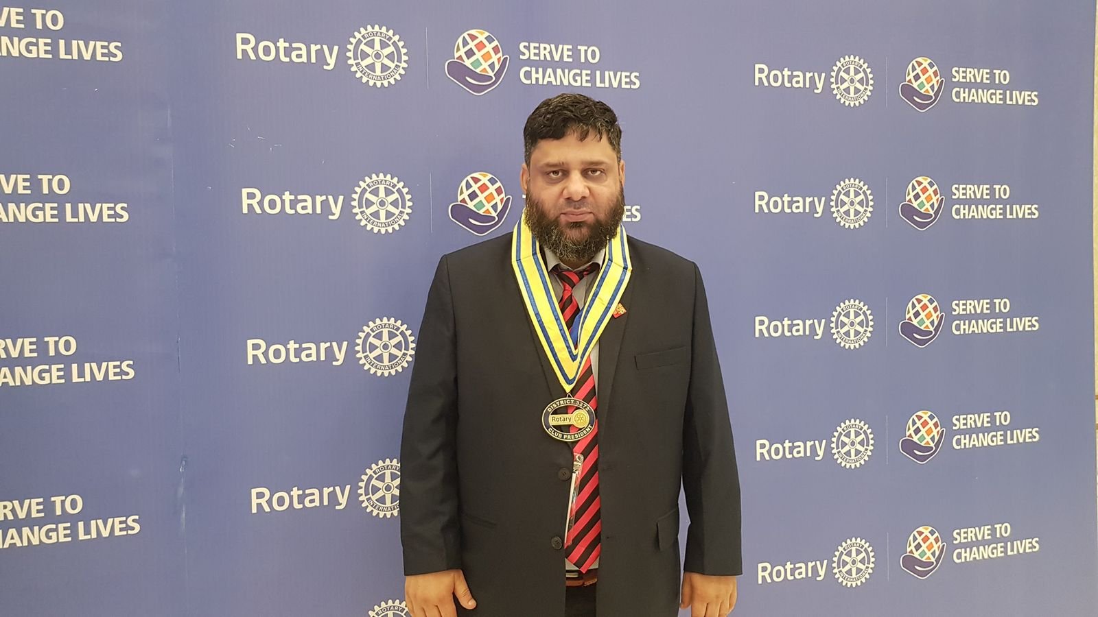 Dr. Ahmed Ejaz wearing the club president collar in front of a Serve to Change Lives backdrop