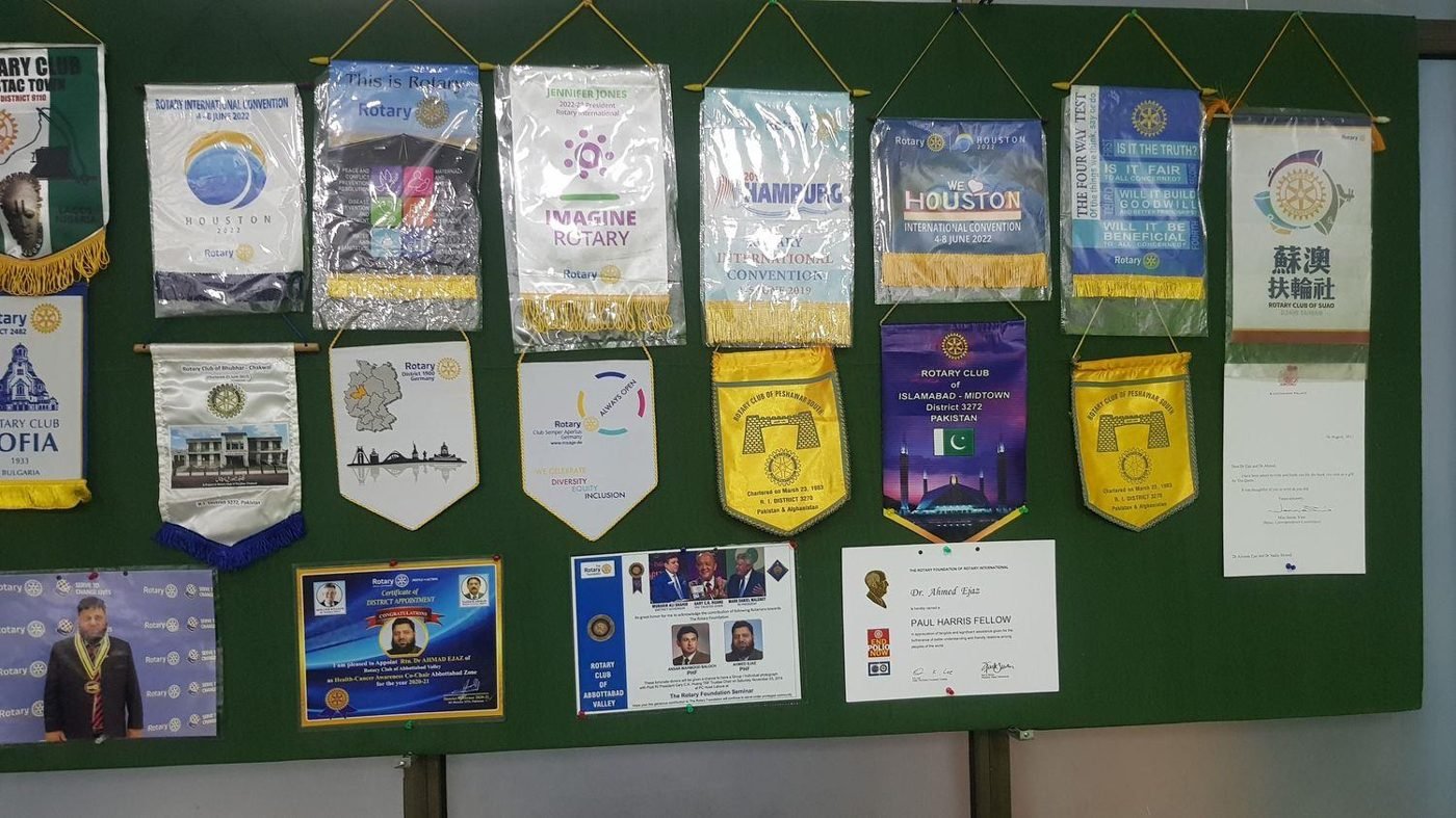 A board of Rotary club banners from around the world with Dr. Ahmed Ejaz's Rotary certificates